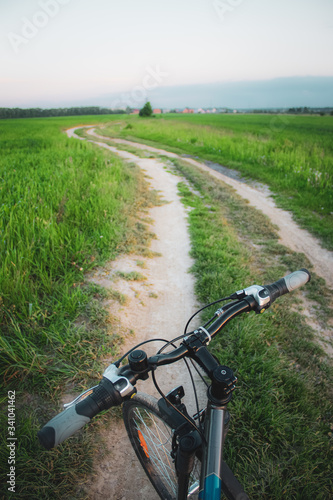 Bicycle steering wheel and gravel road in green summer field