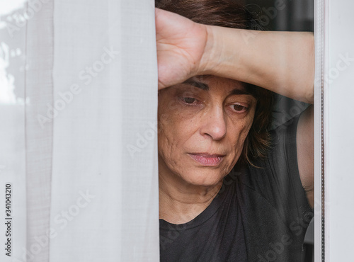 Canvas Print Sad, worried woman looking through the window while there's a quarantine state a