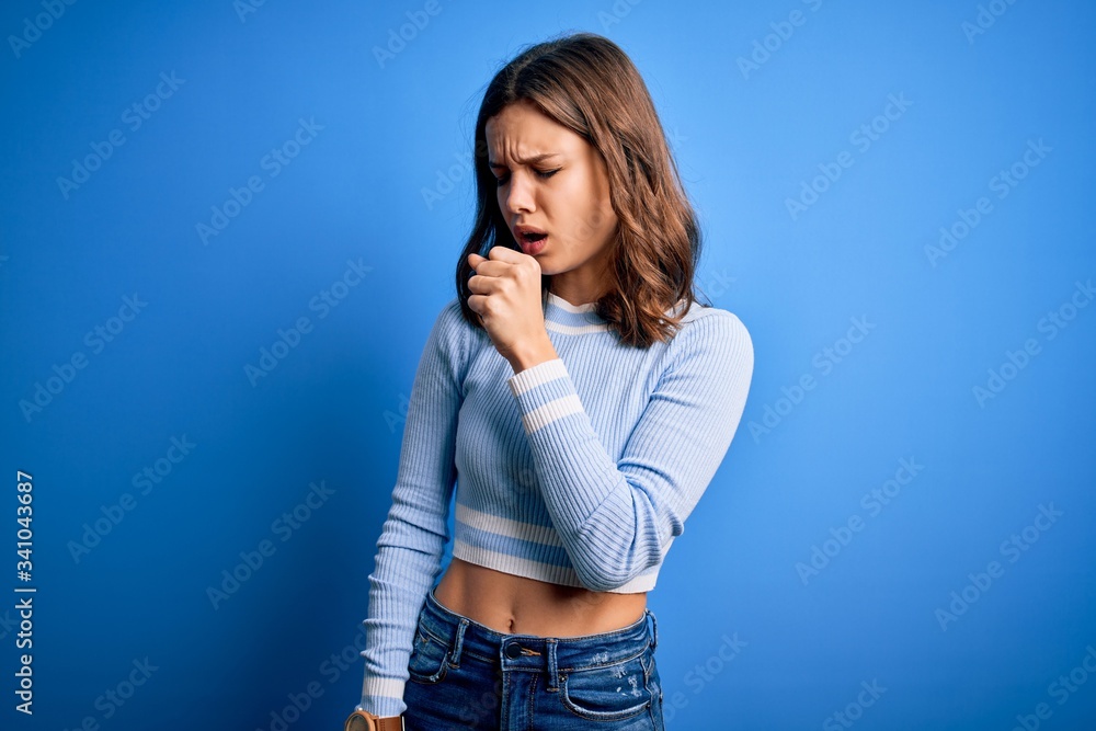 Young beautiful blonde girl wearing casual sweater standing over blue isolated background feeling unwell and coughing as symptom for cold or bronchitis. Health care concept. Young beautiful blonde girl wearing casual sweater standing over blue isolated background feeling unwell and coughing as symptom for cold or bronchitis. Health care concept.