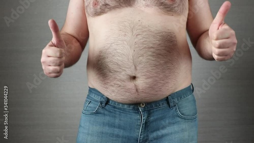 Happy shirtless fat man in jeans showing thumbs up and dancing in slow motion. Big obese belly shaking. Overeating problem concept