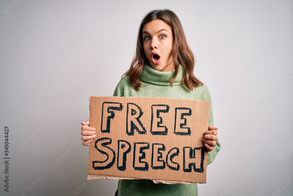 Young blonde girl holding protest banner with free speech message as rights freedom scared in shock with a surprise face, afraid and excited with fear expression Young blonde girl holding protest banner with free speech message as rights freedom scared in shock with a surprise face, afraid and excited with fear expression