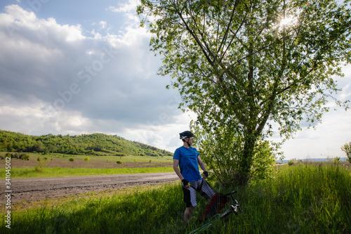 Man with bicycle in full cycling equipment with helmet, blue t-shirt in green summer field, active healthy lifestyle in nature envirment