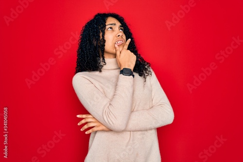 Young african american curly woman wearing casual turtleneck sweater over red background Thinking worried about a question, concerned and nervous with hand on chin © Krakenimages.com