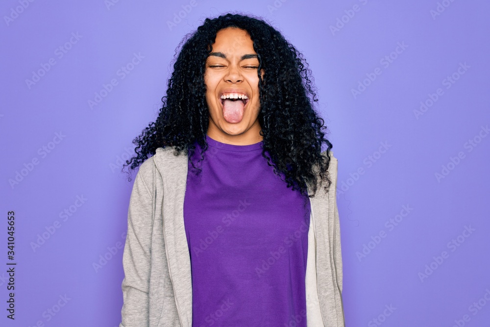 Young african american sporty woman wearing casual sweatshirt over purple background sticking tongue out happy with funny expression. Emotion concept. Young african american sporty woman wearing casual sweatshirt over purple background sticking tongue out happy with funny expression. Emotion concept.