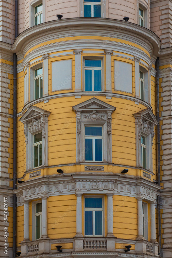 Fragment of the facade of an old building in the shape of a round tower with windows framed by stucco patterns Fragment of the facade of an old building in the shape of a round tower with windows framed by stucco patterns
