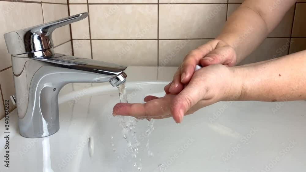 woman washes her hands in the bathroom in a white ceramic sink under the tap, the concept of cleanliness and hygienic routine woman washes her hands in the bathroom in a white ceramic sink under the tap, the concept of cleanliness and hygienic routine