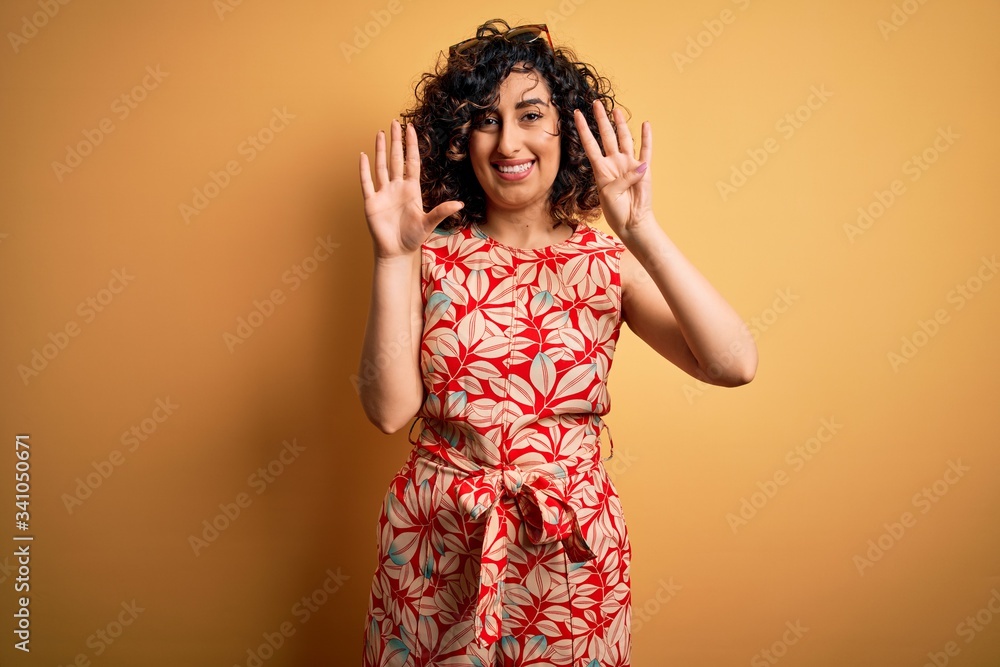 Young beautiful curly arab woman on vacation wearing summer floral dress and sunglasses showing and pointing up with fingers number nine while smiling confident and happy. Young beautiful curly arab woman on vacation wearing summer floral dress and sunglasses showing and pointing up with fingers number nine while smiling confident and happy.