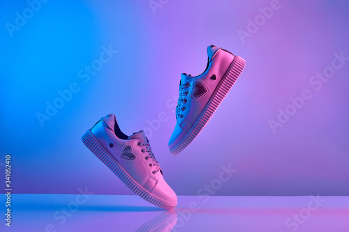 Obraz na plátně Trendy white teenage sneakers flying in trendy neon light