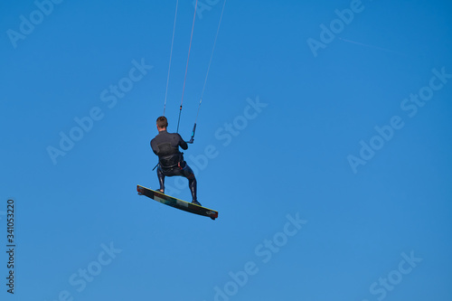 Kitesurfer in wetsuit in the jump on a background of blue sky