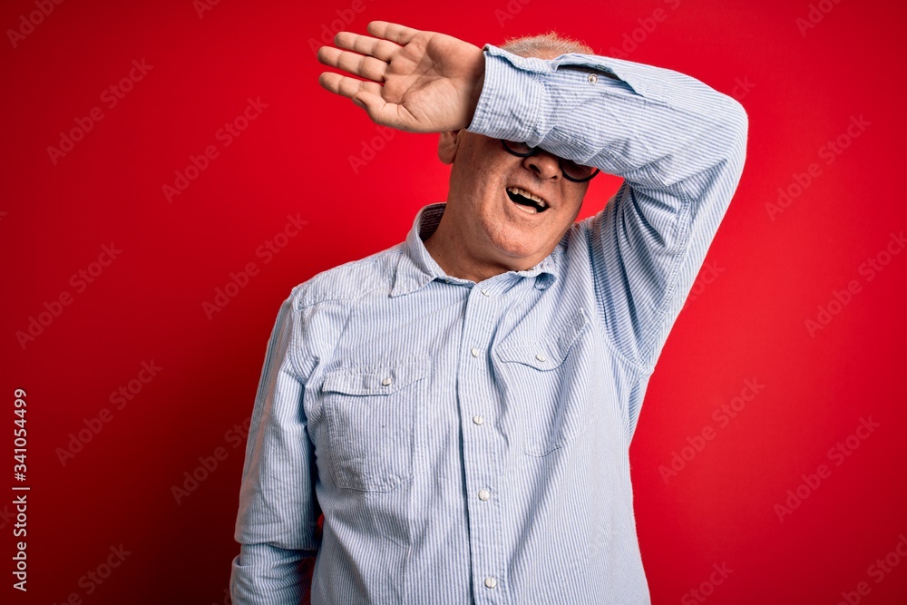 Middle age handsome hoary man wearing casual striped shirt and glasses over red background covering eyes with arm smiling cheerful and funny. Blind concept.