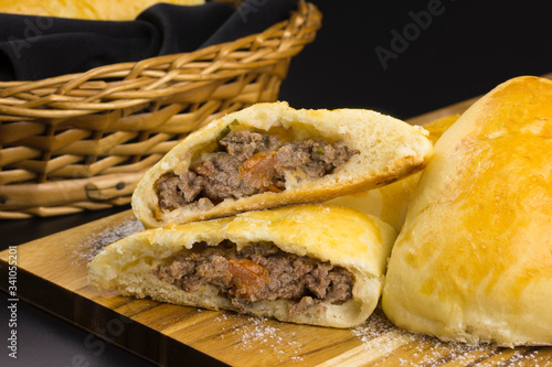 Syrian-Lebanese pie stuffed with meat called sfiha with one open in a cutting board in black background