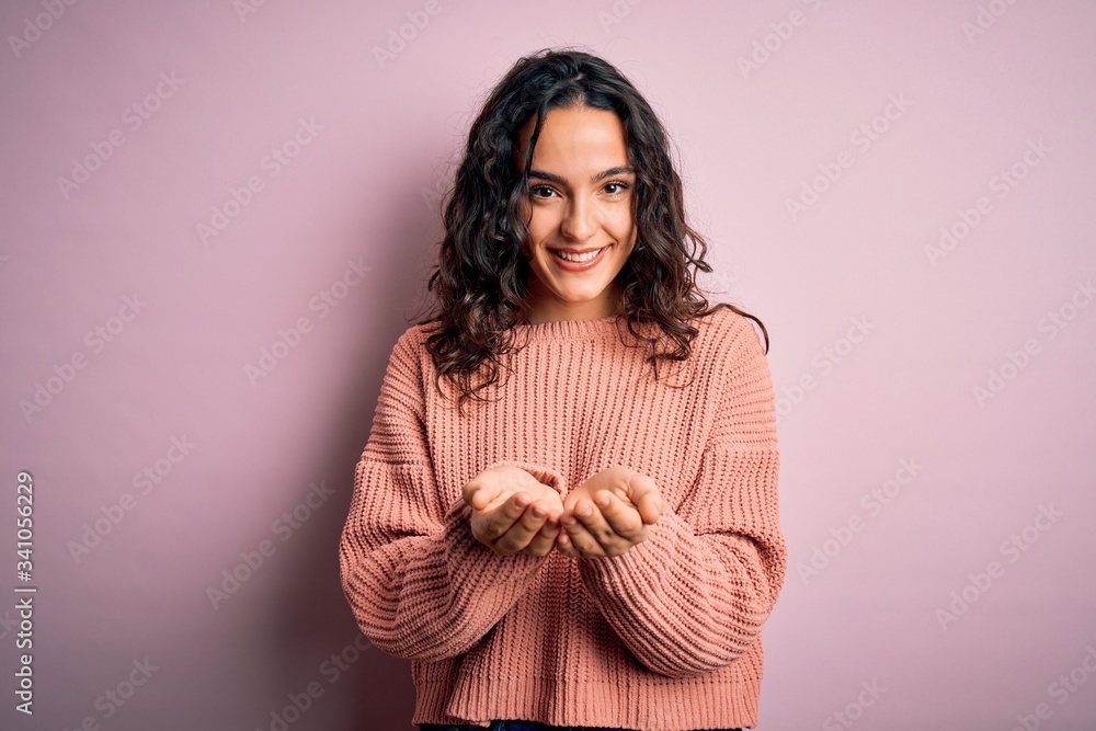 Young beautiful woman with curly hair wearing casual sweater over isolated pink background Smiling with hands palms together receiving or giving gesture. Hold and protection Young beautiful woman with curly hair wearing casual sweater over isolated pink background Smiling with hands palms together receiving or giving gesture. Hold and protection