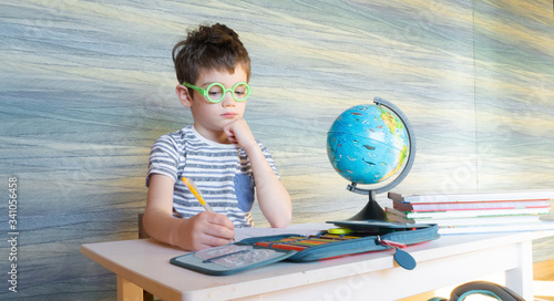 Photography Little egghead schoolboy is doing homework in geography