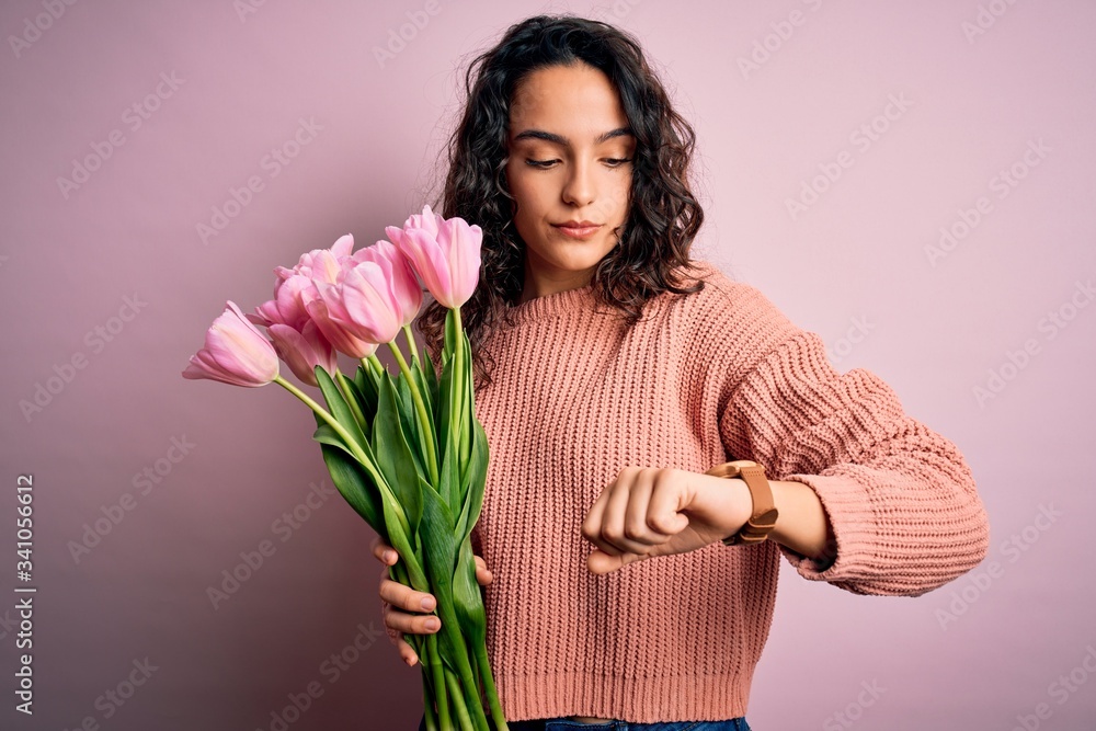 Young beautiful romantic woman with curly hair holding bouquet of pink tulips Checking the time on wrist watch, relaxed and confident Young beautiful romantic woman with curly hair holding bouquet of pink tulips Checking the time on wrist watch, relaxed and confident