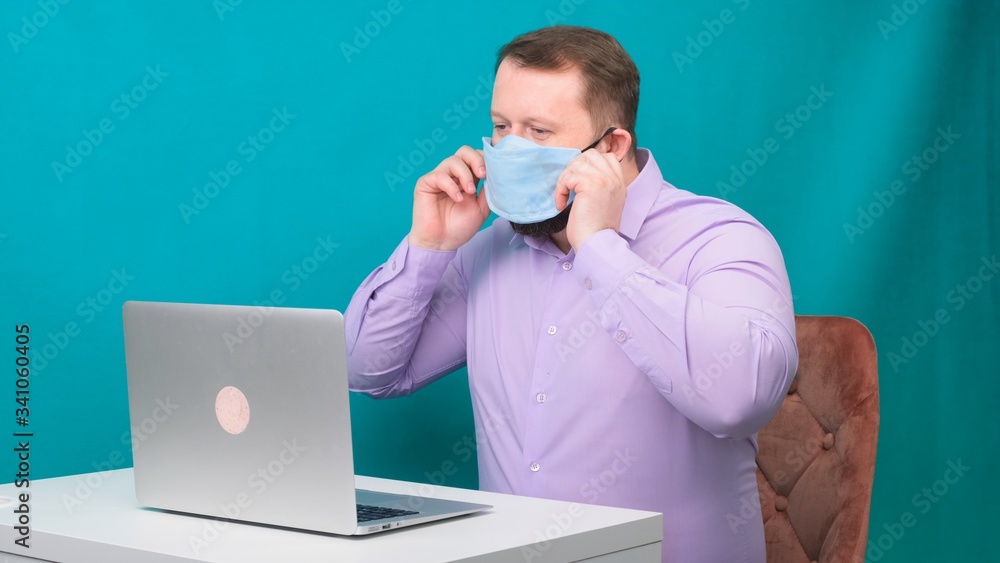 Portrait of bearded man in a purple shirt is wearing a protective medical mask to work at a laptop at home on a green background. Quarantine concept Portrait of bearded man in a purple shirt is wearing a protective medical mask to work at a laptop at home on a green background. Quarantine concept
