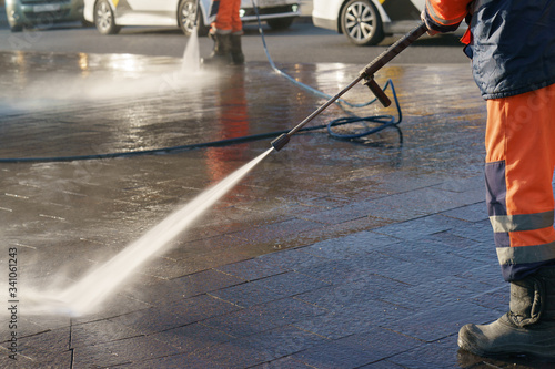 Worker watering from a hose outdoor. Using water. Jet spray of water in sunlight, Concept of freshness, street cleaning in Coronavirus Pandemic reality. 