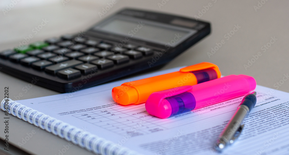 Colorful markers and pen on the background of the graph and document.  Finance. Calculator, notebooks, colored paper clips, markers.