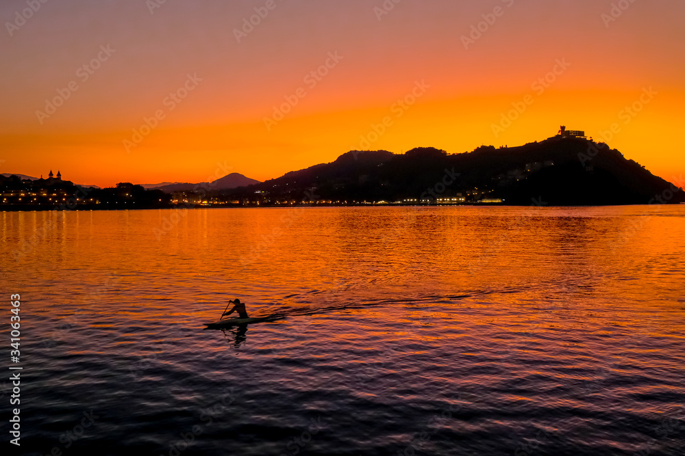 Fototapeta premium Sunset on Mount Igueldo and and man with a paddle in koyak in Donosti San Sebastian, Basque Country, northern spain