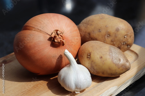 Onion  garlic and potatoes on chopping board 