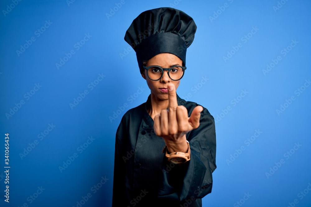 Young african american chef woman wearing cooker uniform and hat over blue background Showing middle finger, impolite and rude fuck off expression Young african american chef woman wearing cooker uniform and hat over blue background Showing middle finger, impolite and rude fuck off expression