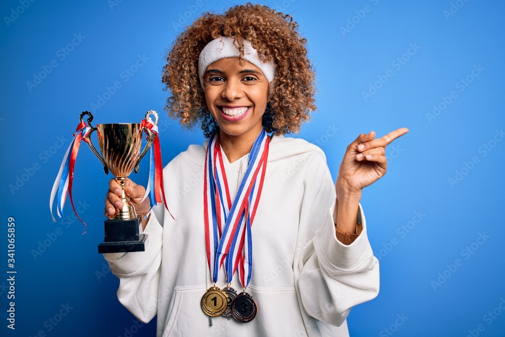 Young african american sporty woman doing sport winning medals and trophy very happy pointing with hand and finger to the side