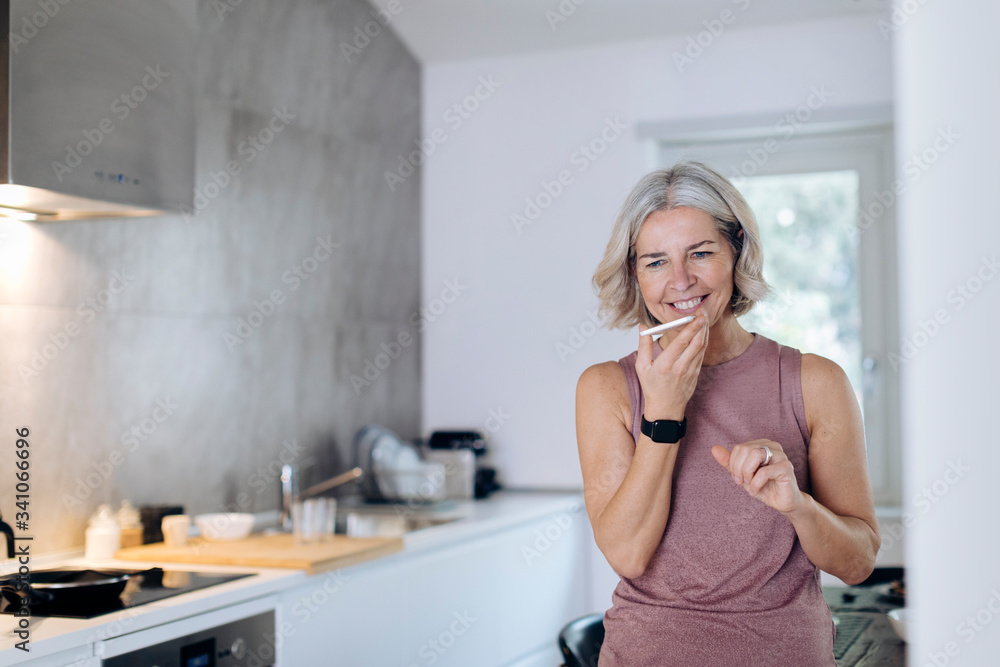 Mature woman using cell phone in kitchen at home Mature woman using cell phone in kitchen at home