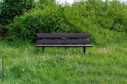 Frontansicht einer Parkbank mitten in der grünen Natur an einem Feldweg