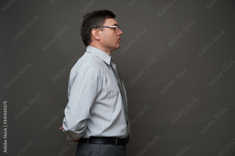 a man dressed as a businessman posing in a studio on a gray background, glasses, a light striped shirt and tie - casual office wear