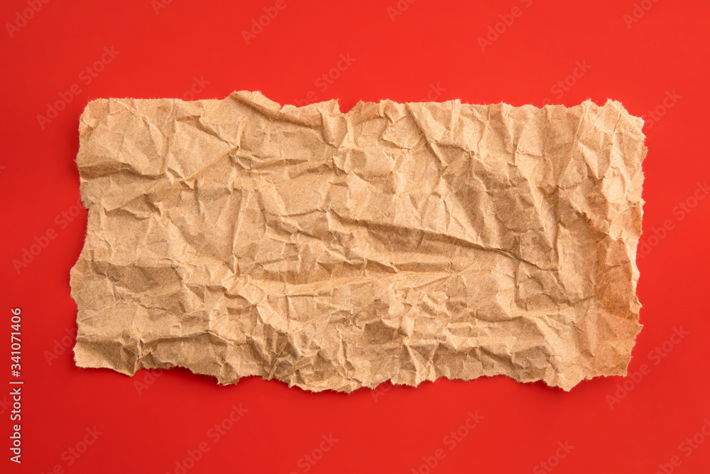 Empty crumpled piece of recycled paper on red background