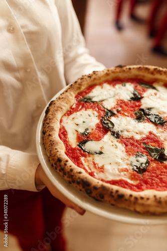 Waiter with pizza Margherita in hands. Close-up view pizza margarita in authentic Italian pizzeria. Original recipe. Cafe backdrop photo