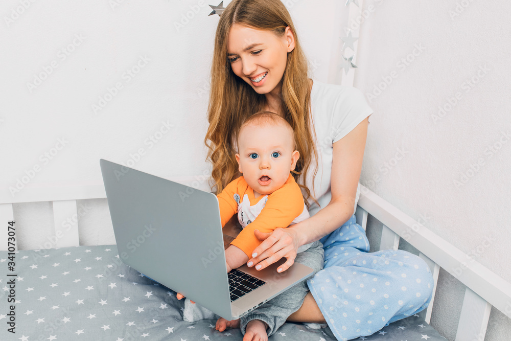 Young mother in pajamas with a small child, relaxing sitting on the bed, with a portable laptop Young mother in pajamas with a small child, relaxing sitting on the bed, with a portable laptop