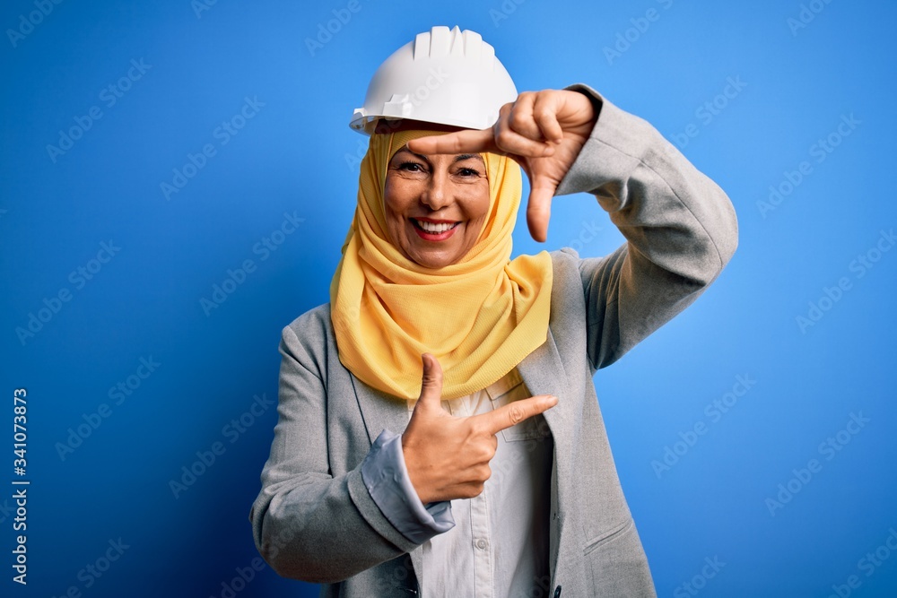 Middle age brunette architect woman wearing muslim traditional hijab and security helmet smiling making frame with hands and fingers with happy face. Creativity and photography concept. Middle age brunette architect woman wearing muslim traditional hijab and security helmet smiling making frame with hands and fingers with happy face. Creativity and photography concept.