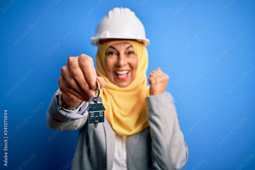 Middle age architect woman wearing muslim hijab and security helmet holding home keys screaming proud and celebrating victory and success very excited, cheering emotion Middle age architect woman wearing muslim hijab and security helmet holding home keys screaming proud and celebrating victory and success very excited, cheering emotion