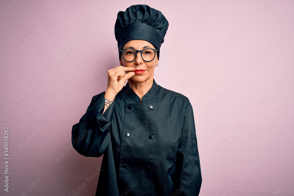 Middle age brunette chef woman wearing cooker uniform and hat over isolated pink background mouth and lips shut as zip with fingers. Secret and silent, taboo talking Middle age brunette chef woman wearing cooker uniform and hat over isolated pink background mouth and lips shut as zip with fingers. Secret and silent, taboo talking
