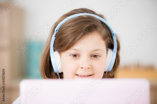 Portrait of a teenage schoolgirl girl in headphones on a pink computer laptop, studies online, enjoys music, uses a video call application, online games, listens to music, reads, e-books. photo