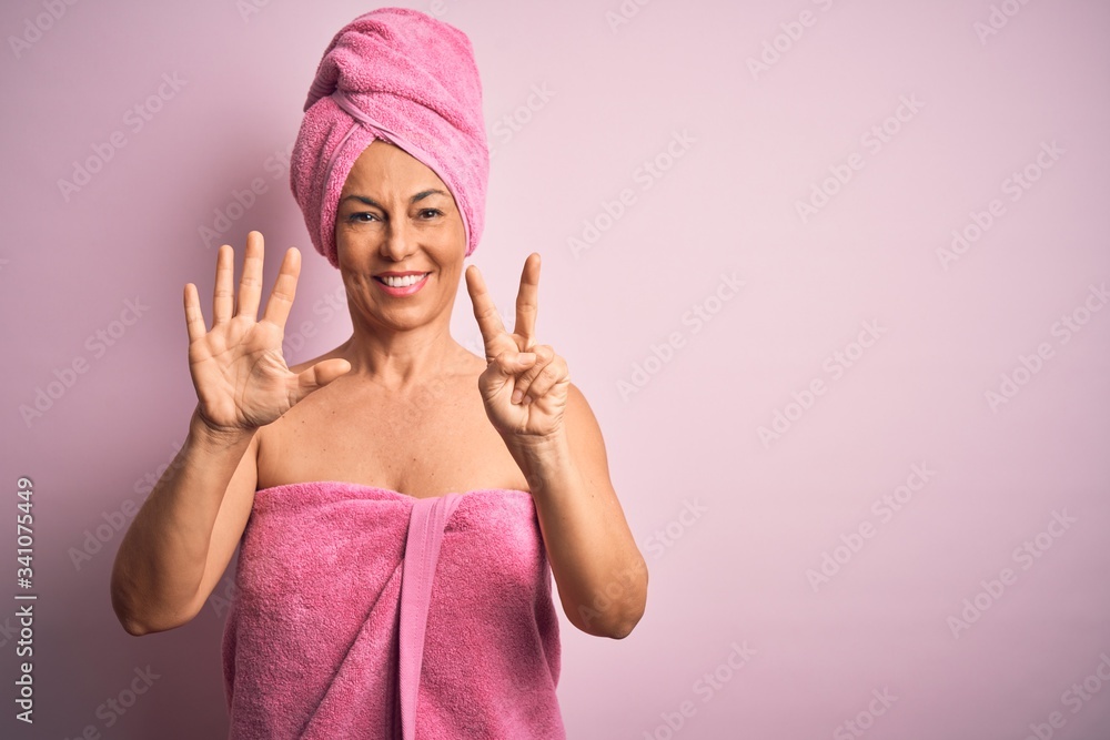 Middle age woman wearing bath towel from beauty body care over pink background showing and pointing up with fingers number seven while smiling confident and happy. Middle age woman wearing bath towel from beauty body care over pink background showing and pointing up with fingers number seven while smiling confident and happy.
