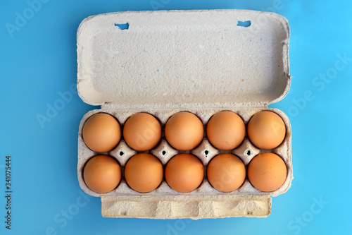 Cardboard tray for ten eggs top view. Brown chicken eggs in a paper box on a blue background. Eggs in a paper container.