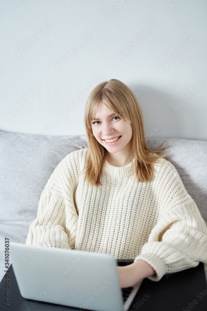 Attractive caucasian blonde using laptop at home for study or work, looking straight to camera, smiling widely. Concept of female student doing homework, working on project online or freelance worker Attractive caucasian blonde using laptop at home for study or work, looking straight to camera, smiling widely. Concept of female student doing homework, working on project online or freelance worker