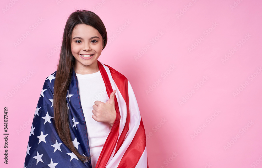 The American Dream. July 4, USA. beautiful girl in a white T-shirt with the American flag, on a pink background. The American Dream. July 4, USA. beautiful girl in a white T-shirt with the American flag, on a pink background.