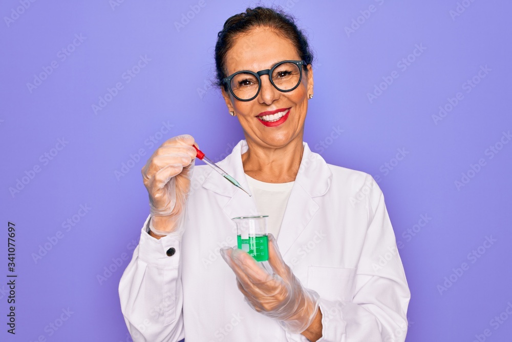 Middle age senior scientist woman wearing laboratory coat holding research test tube with a happy face standing and smiling with a confident smile showing teeth Middle age senior scientist woman wearing laboratory coat holding research test tube with a happy face standing and smiling with a confident smile showing teeth