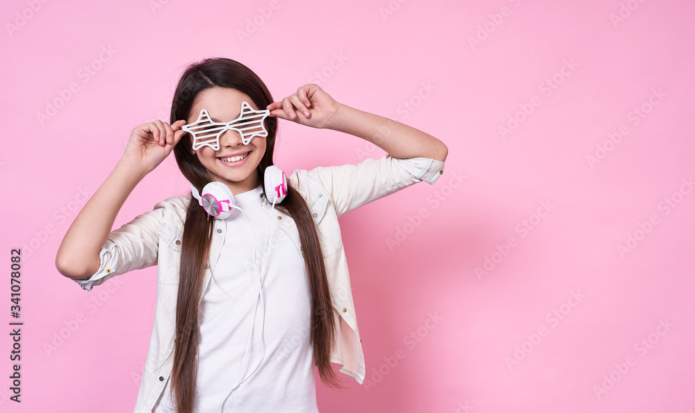 Elegant fun beautiful emotional young girl in stylish glasses, headphones,in a white T-shirt on a pink background. Elegant fun beautiful emotional young girl in stylish glasses, headphones,in a white T-shirt on a pink background.