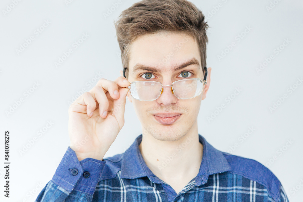Young man in blue shirt and glasses on light grey background. Man holding glasses