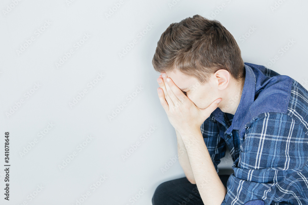A young man covers his face with his hands. Problems and stress. Sad man on a light gray background A young man covers his face with his hands. Problems and stress. Sad man on a light gray background