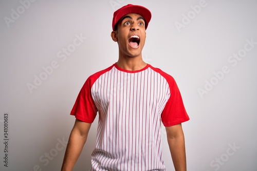 Photography Young handsome african american sportsman wearing striped baseball t-shirt and cap angry and mad screaming frustrated and furious, shouting with anger