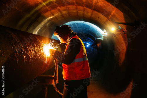 Worker in protective mask welding pipe in tunnel