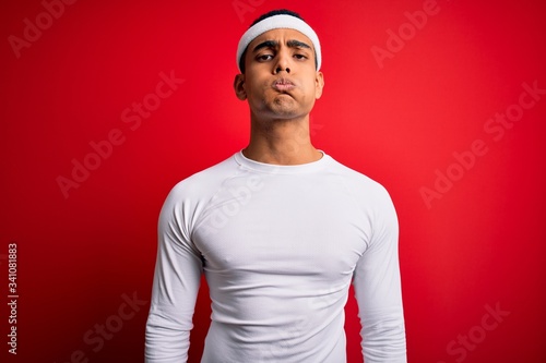 Young handsome african american sportsman wearing sportswear over red background puffing cheeks with funny face. Mouth inflated with air, crazy expression.