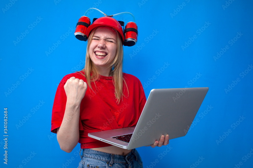 funny girl a fan in a red uniform and a beer hat watches the game on the laptop and enjoy the victory, the cheerleader is rooting for the team funny girl a fan in a red uniform and a beer hat watches the game on the laptop and enjoy the victory, the cheerleader is rooting for the team