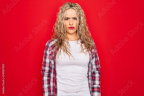 Young beautiful blonde woman wearing casual shirt standing over isolated red background depressed and worry for distress, crying angry and afraid. Sad expression.