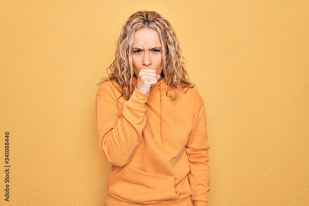 Young beautiful blonde sporty woman wearing casual sweatshirt over yellow background feeling unwell and coughing as symptom for cold or bronchitis. Health care concept.