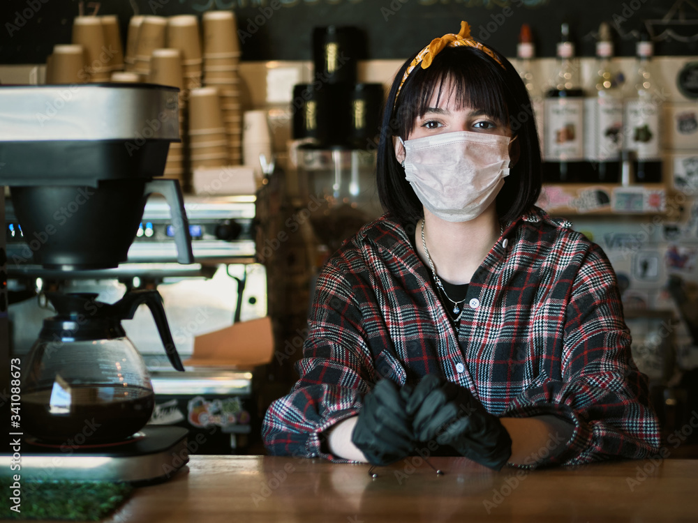 Concept of biohazard security and social responsibility in coronavirus epidemic measures to contain virus spread: young barista girl in medical mask and medical gloves with city cafe background